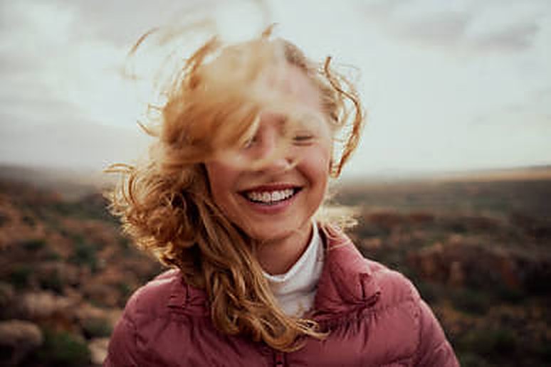 A smiling woman with wind-blown hair outdoors